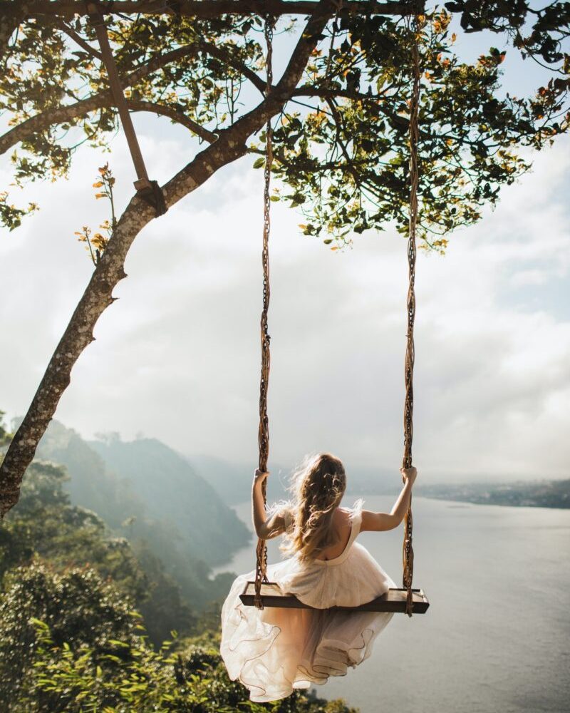 Woman swinging outdoors over amazing mountain, jungle and lake view over a cliff in Bali